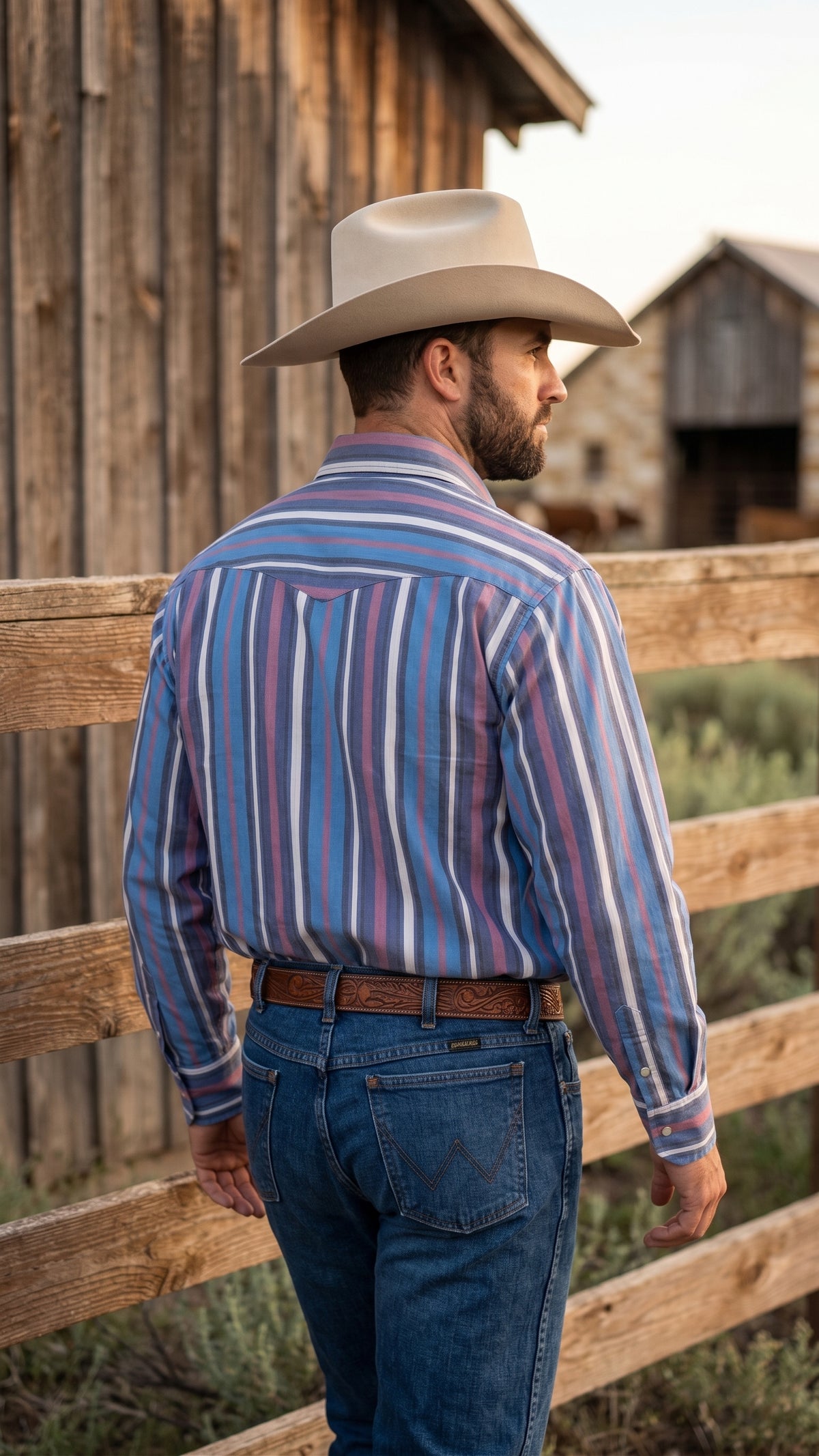 Back view of man wearing blue striped Western snap shirt with Western yoke at a ranch fence
