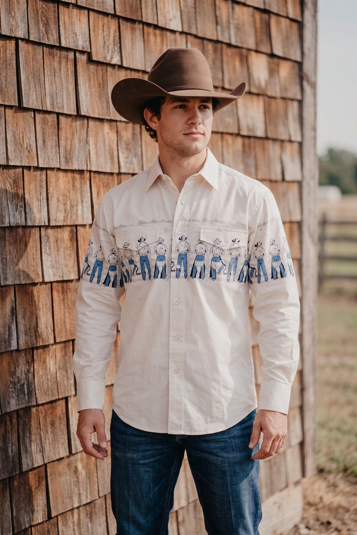 Front view of men's cream pearl snap western shirt showing the continuous cowboy graphic band and chest pockets
