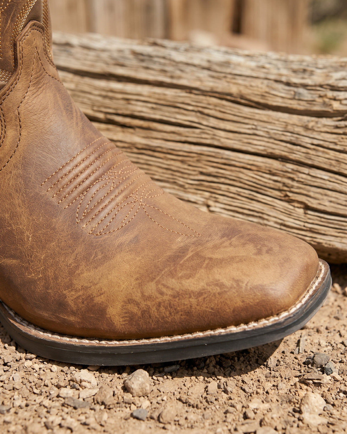 Close-up of distressed tan leather square toe cowboy boot showing toe stitching and welt construction